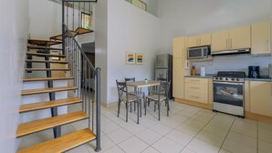 A modern kitchen with a built-in oven, microwave, and stove. There is a dining area with a table and chairs, and a staircase with wooden steps and metal railings.