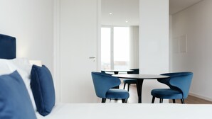 A modern hotel room with a bed, a desk, and a dining area with blue chairs and a table. - Feel Porto Lapa Collection Flat 3 1 (Porto)