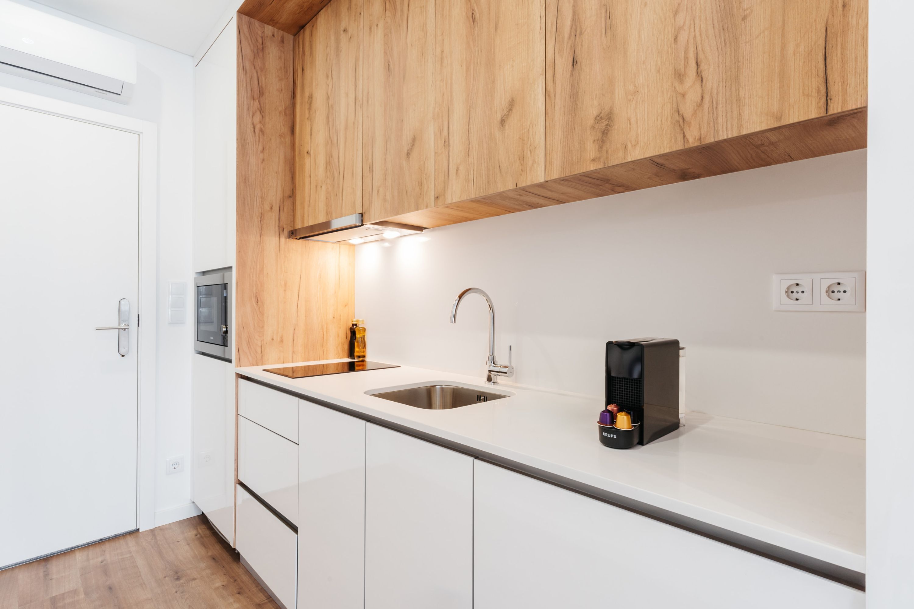 Een moderne keuken met witte kasten, een roestvrijstalen spoelbak, houten plafond en een koffieapparaat.