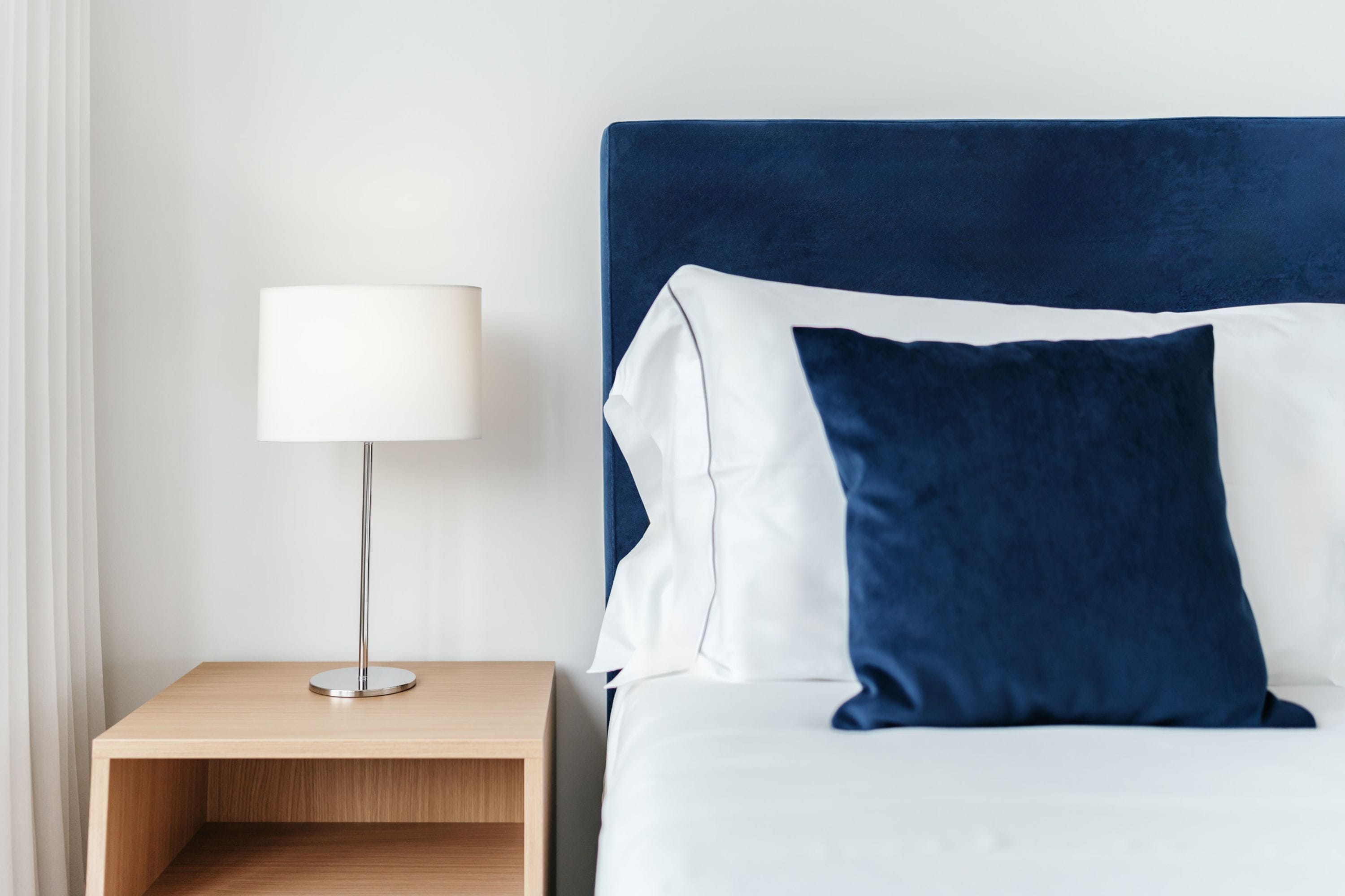 A neatly made bed with a blue headboard, a white pillow, and a bedside table with a lamp.