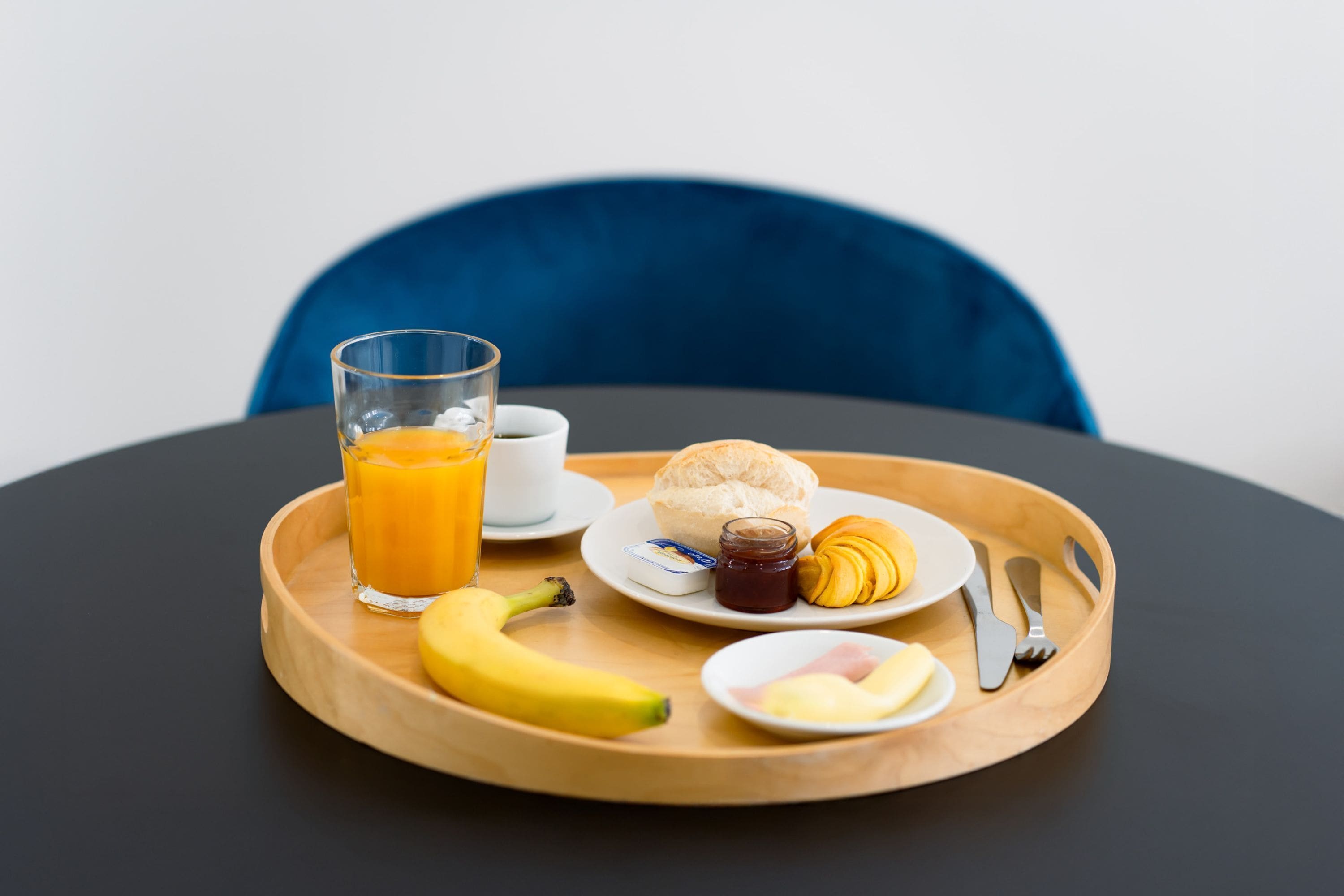 Un plateau de petit-déjeuner avec une banane, du jus d’orange, un croissant, du jambon et la moitié d’un autre croissant, le tout posé sur un plateau en bois.