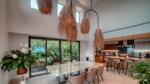 A modern kitchen with a large island, pendant lights, and a view of greenery outside.