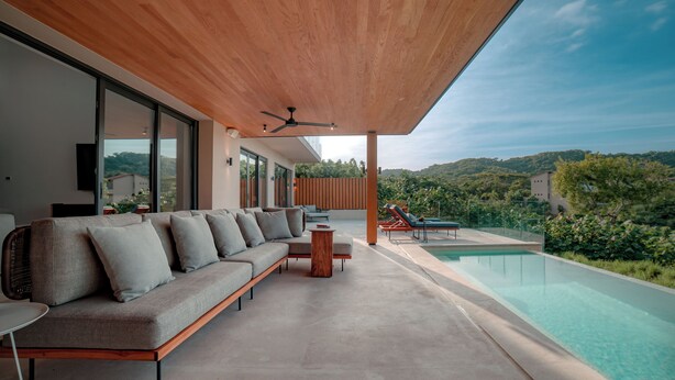 A modern outdoor living area with a long sofa, a small round table, and a pool.