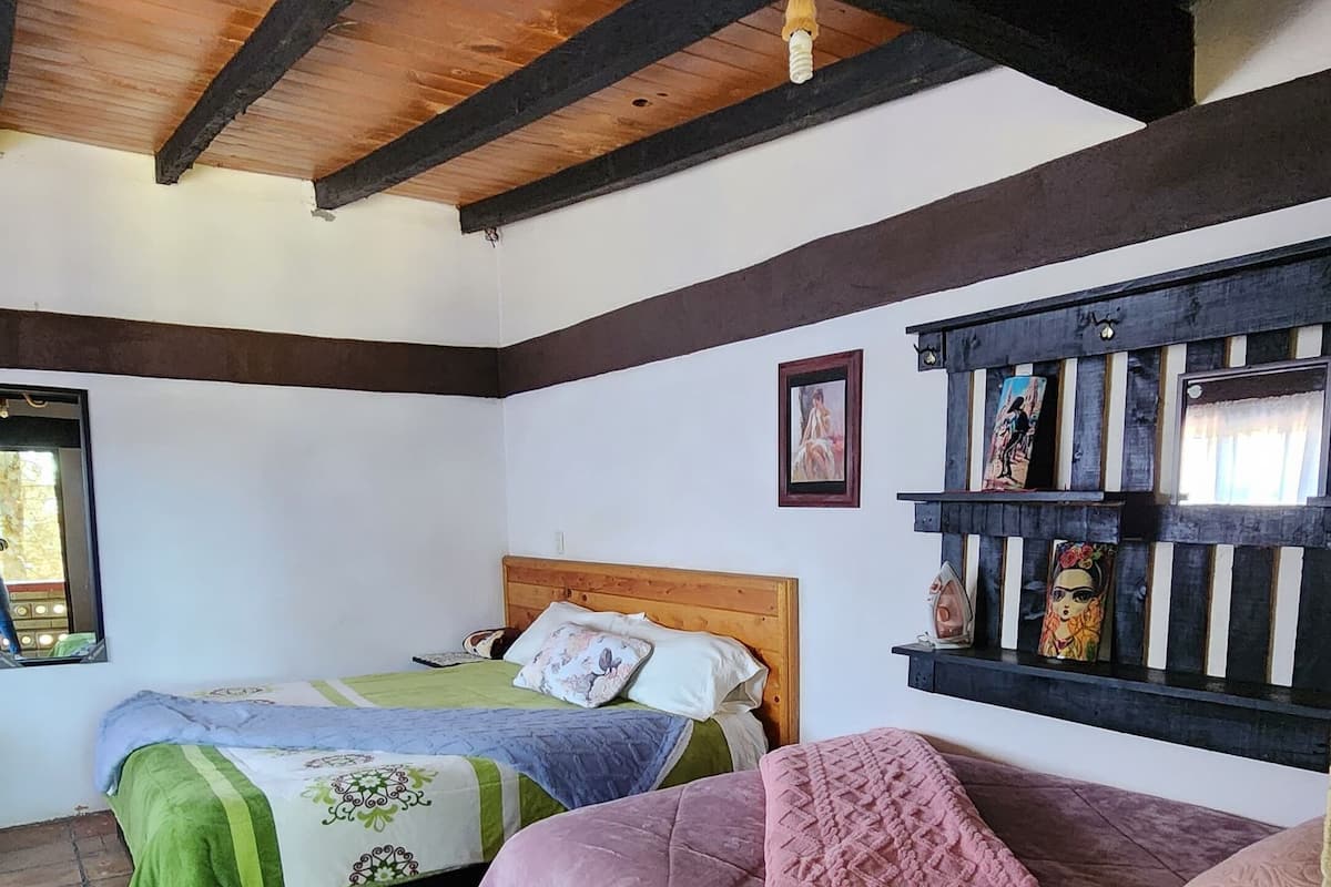 A bedroom with two beds, a wooden ceiling, a brick floor, and a shelf with decorative items.