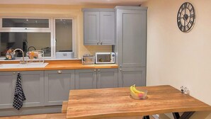 Une cuisine moderne avec des meubles gris, un plan de travail en bois, un four à micro-ondes et une horloge au mur.