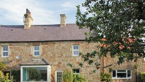 Une maison en pierre avec un toit en briques, une grande fenêtre et un jardin à l’avant.