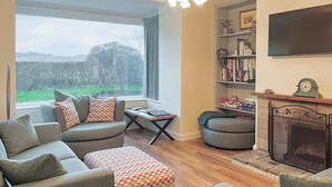 Un salon chaleureux avec un ensemble de canapés, un pouf à motifs, une cheminée et une bibliothèque.