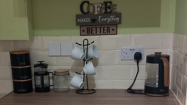 A kitchen counter with coffee-making equipment, including a coffee maker, a French press, and a mug rack.