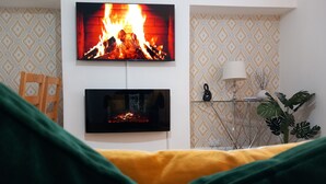 A living room with a fireplace, a television, and a side table with a lamp and plant.
