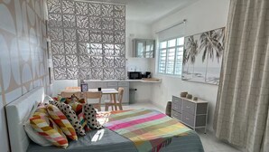 A modern bedroom with a bed, a desk, and a chair. There is a window with a view of palm trees.