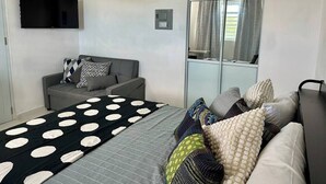 A modern bedroom with a bed, a sofa, a TV, and a large window.