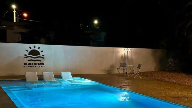 A swimming pool with lounge chairs and a wall with the text "Beachtown Luxury Villas".