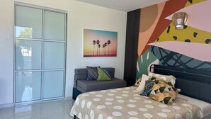 Un dormitorio moderno con cama, sofá, puerta de cristal y una pared con arte abstracto.