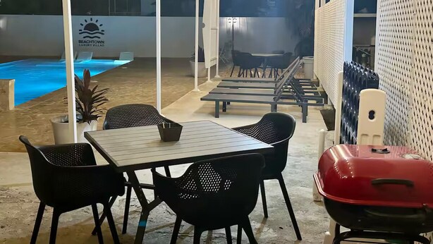 Un patio al aire libre con piscina, una parrilla y una mesa con sillas.