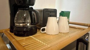 Una cafetera, dos tazas blancas, un bolso verde y una cafetera Hamilton Beach sobre una mesa de madera.