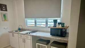 Cocina compacta con un fregadero, un microondas y dos taburetes de bar.