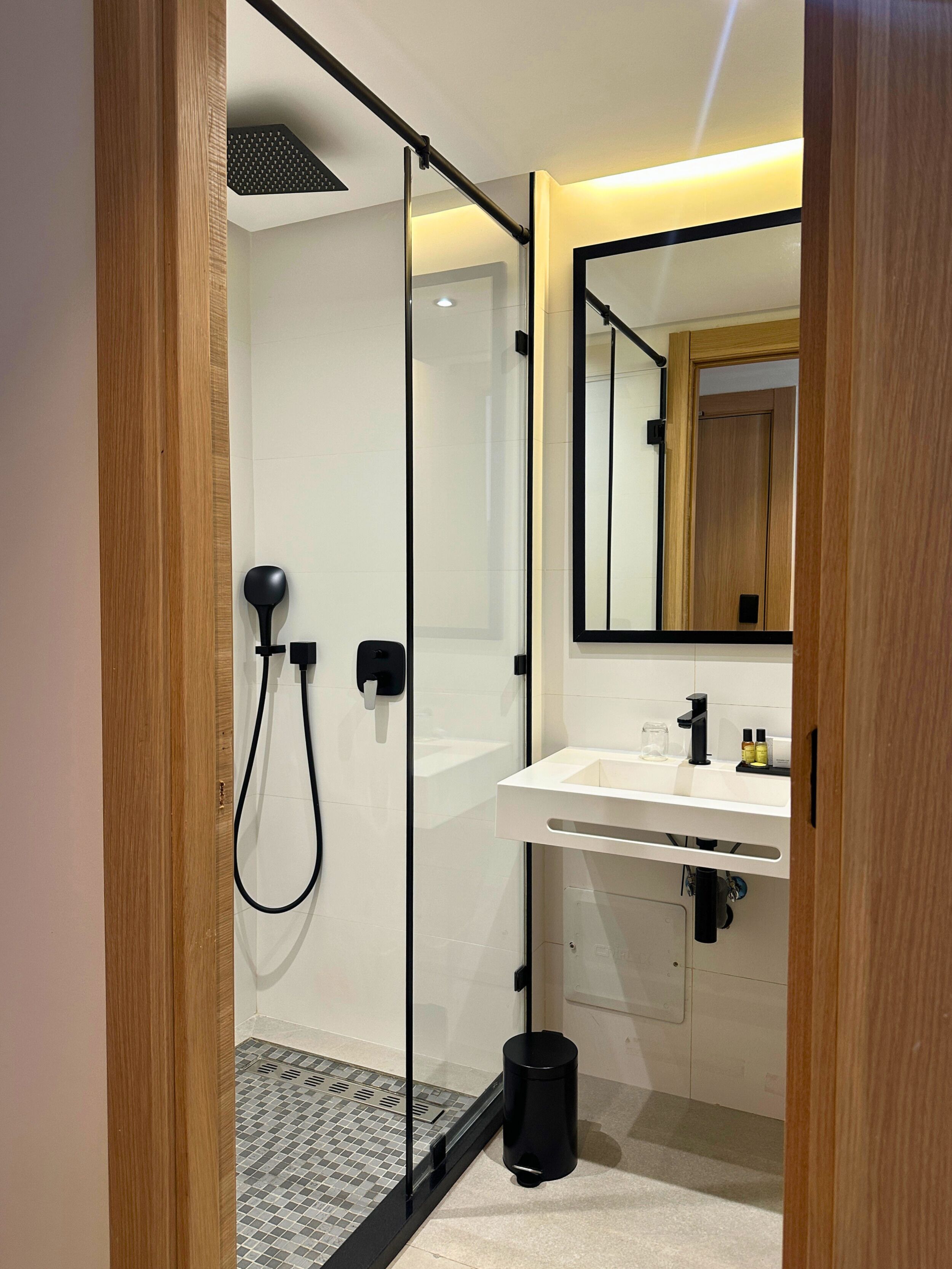 A modern bathroom with a glass shower enclosure, a white sink, and a mirror above the sink.