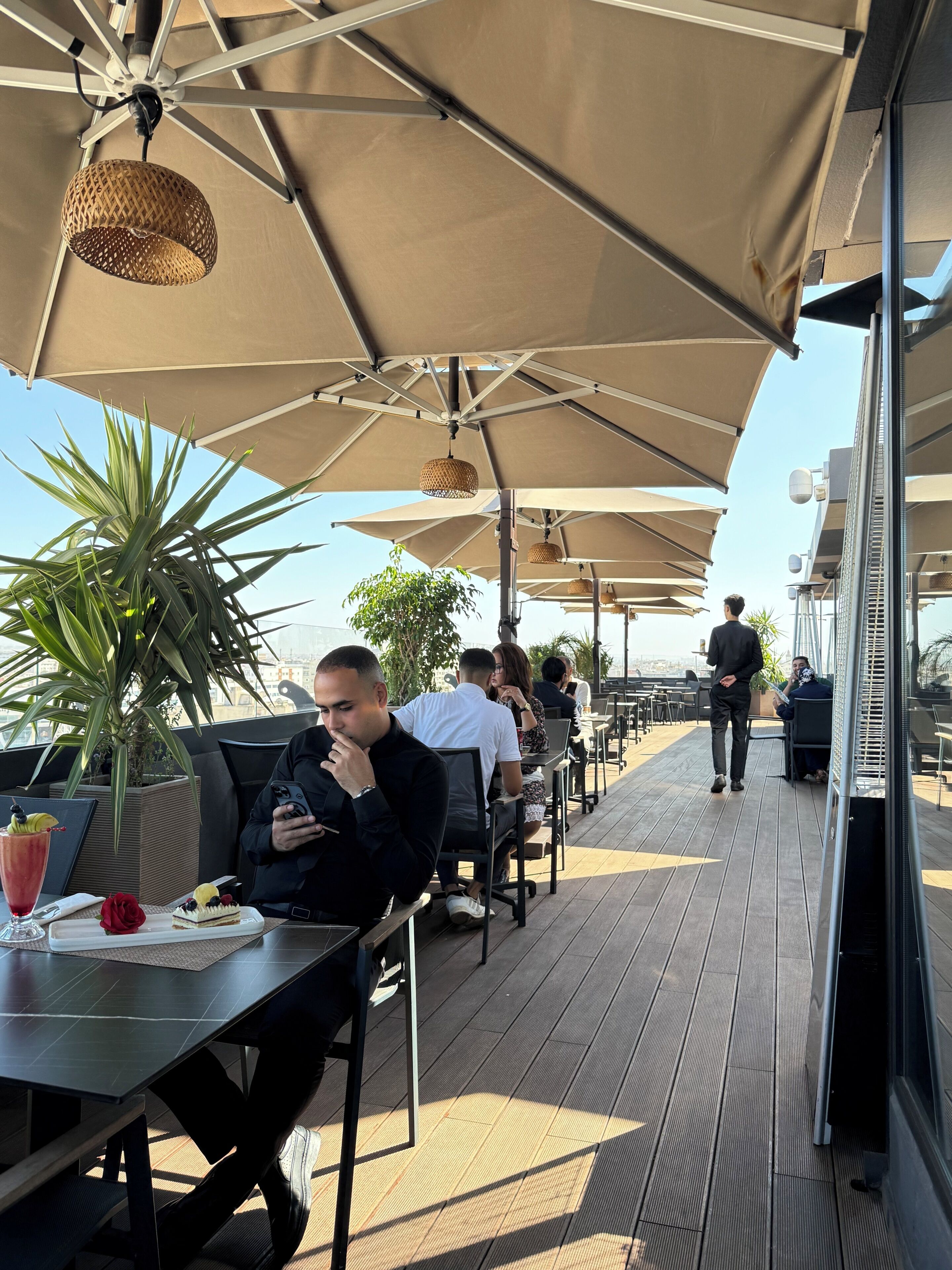 Un área de comedor al aire libre con mesas, sillas y sombrillas.