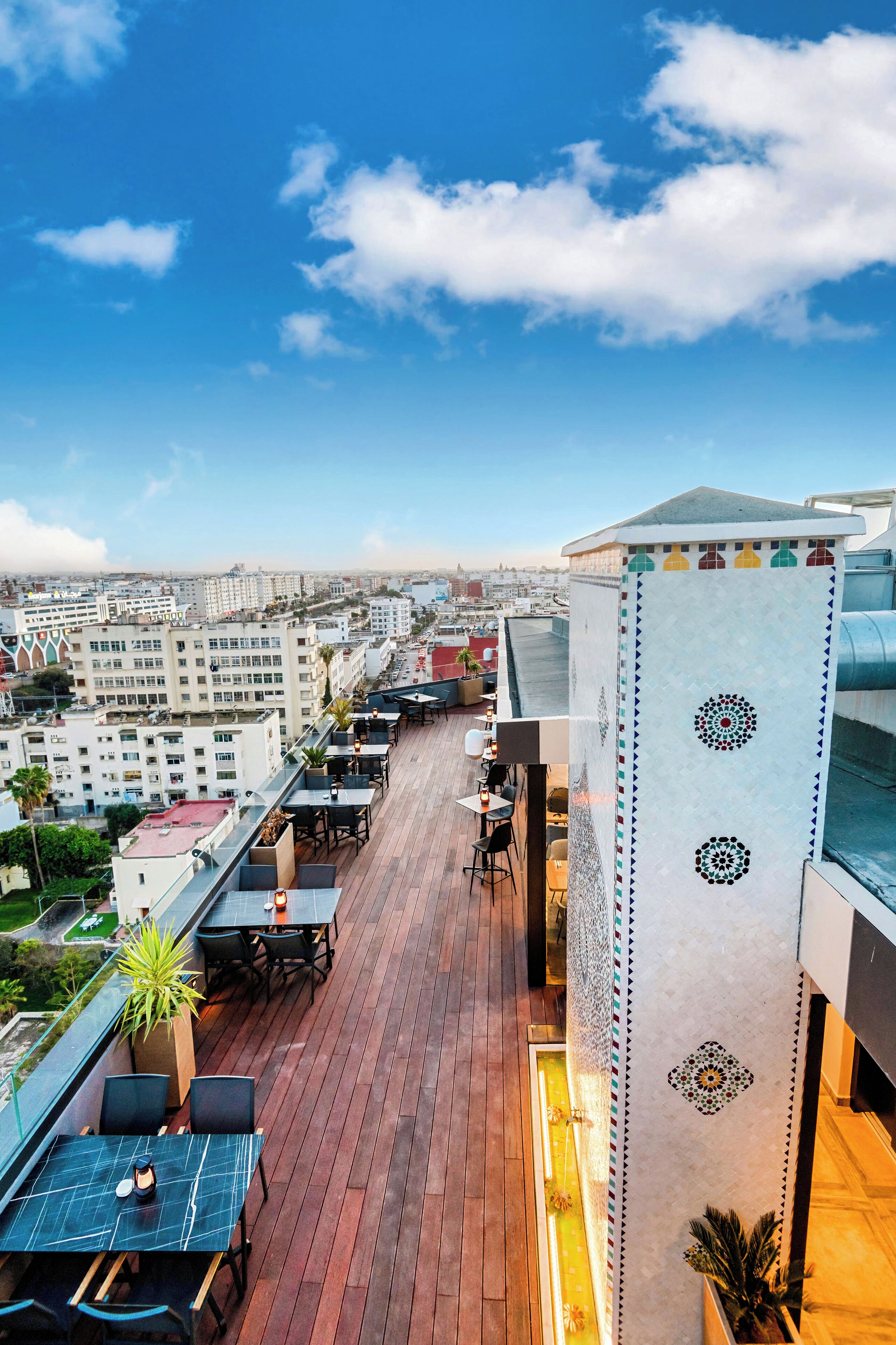 Una terraza en la azotea con mobiliario exterior, vistas panorámicas de la ciudad y una pared decorativa con patrones geométricos.