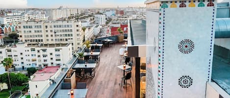 Una terraza en la azotea con mobiliario exterior, vistas panorámicas de la ciudad y una pared decorativa con patrones geométricos.