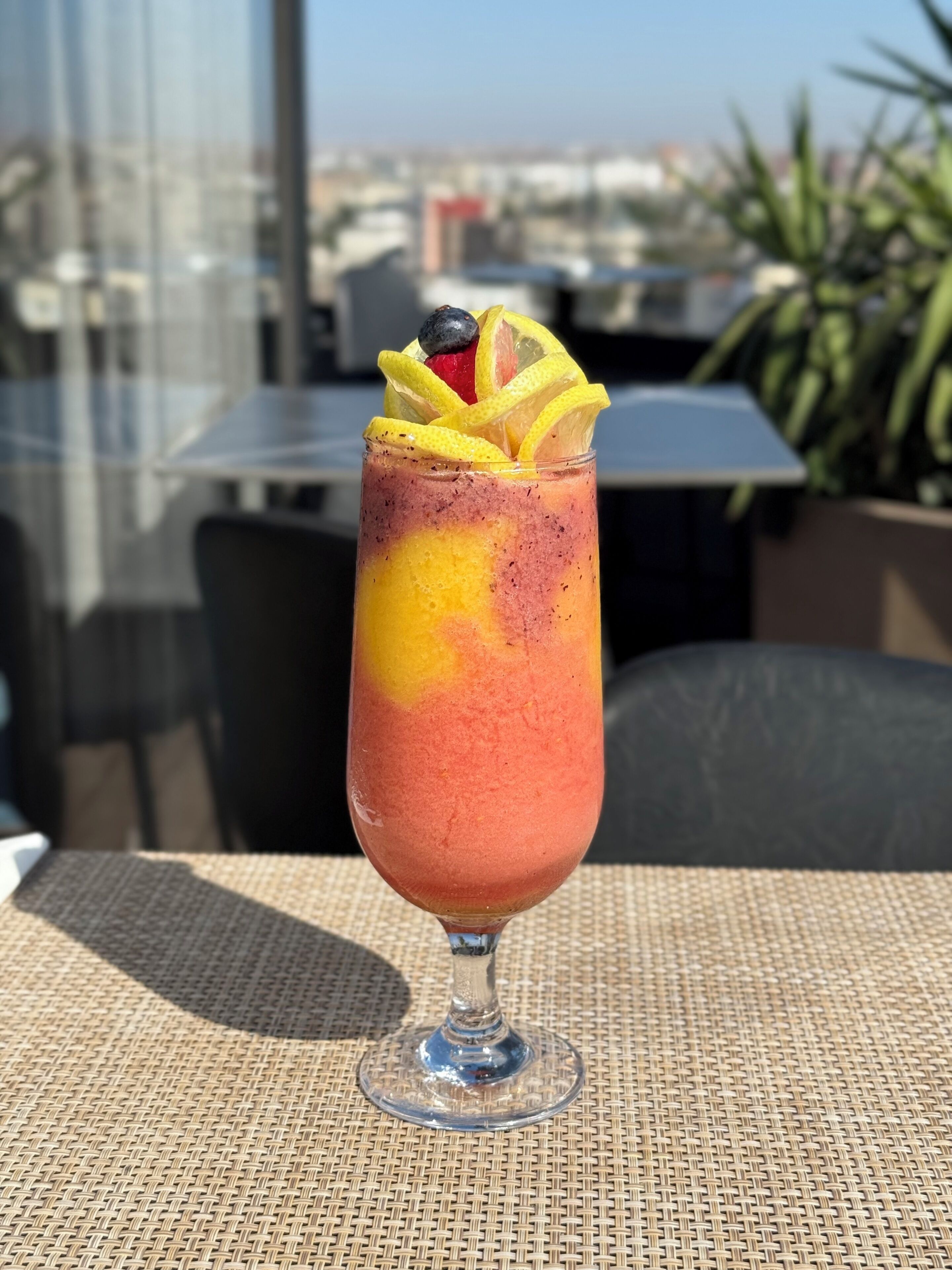 A glass of fruit smoothie with a slice of lemon and a blueberry on top, placed on a woven table mat.