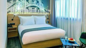Habitación de hotel con una cama grande, una mesita de noche, una pequeña mesa con un plato y un vaso, y una silla.