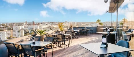 An outdoor terrace with wooden flooring, tables, chairs, and potted plants.