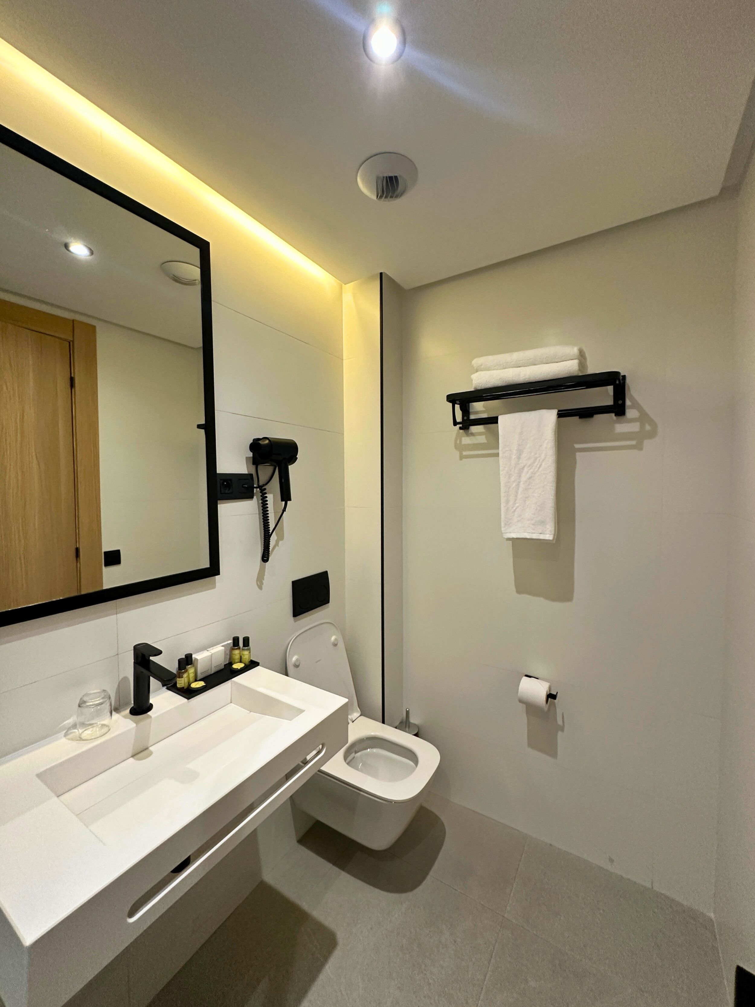 A modern bathroom with a white sink, a toilet, a mirror, and a towel rack.