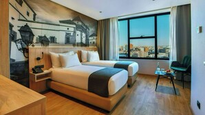 A hotel room with two beds, a large window with a city view, a painting on the wall, and a small table with a bottle and glass. - ADAY Hotel Casablanca (Casablanca)