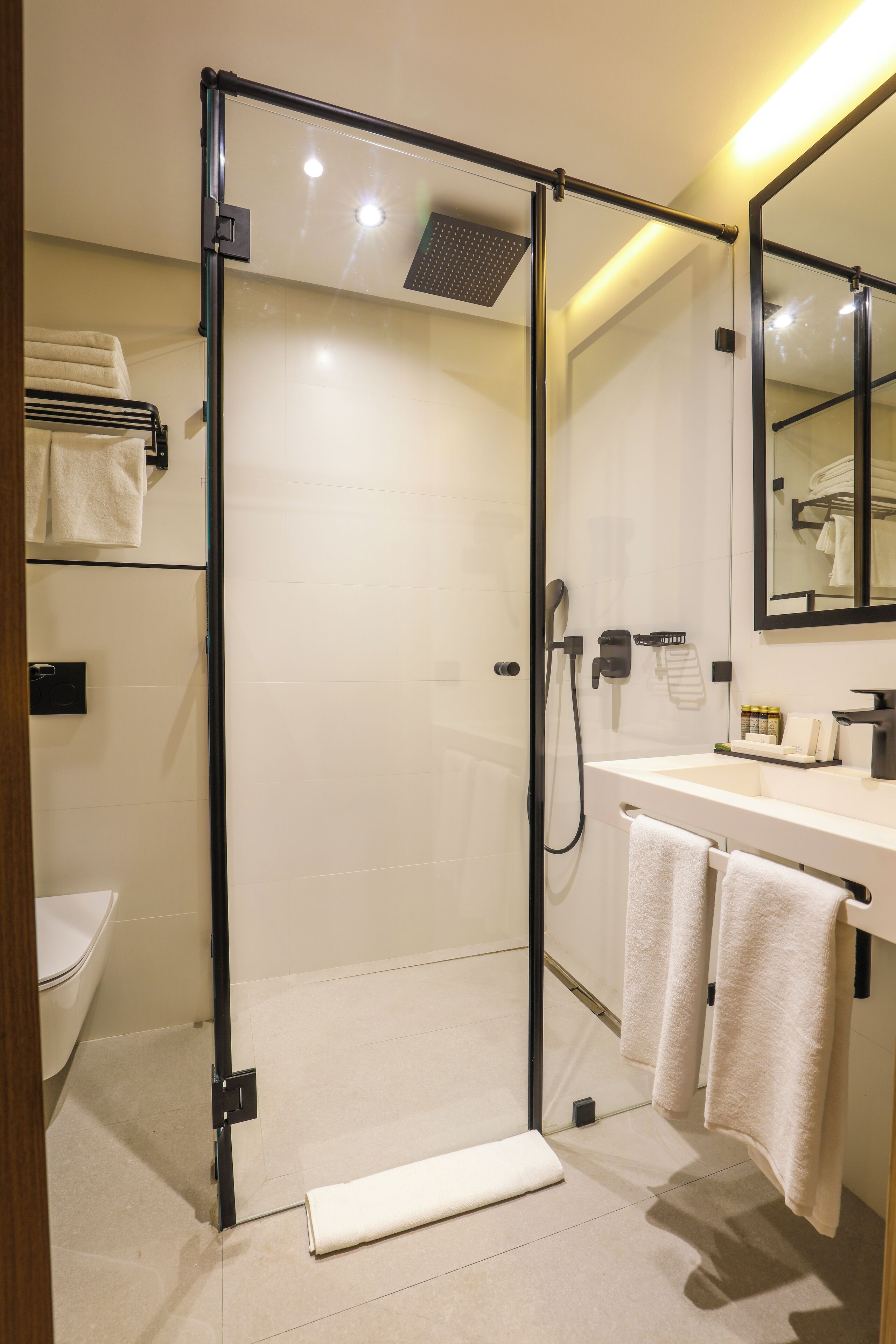 Un baño moderno con ducha envuelta en vidrio, inodoro, lavamanos con toallero y espejo.