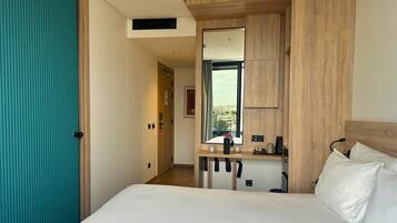 A hotel room with a bed, a mirror, a desk, and a view of the city.