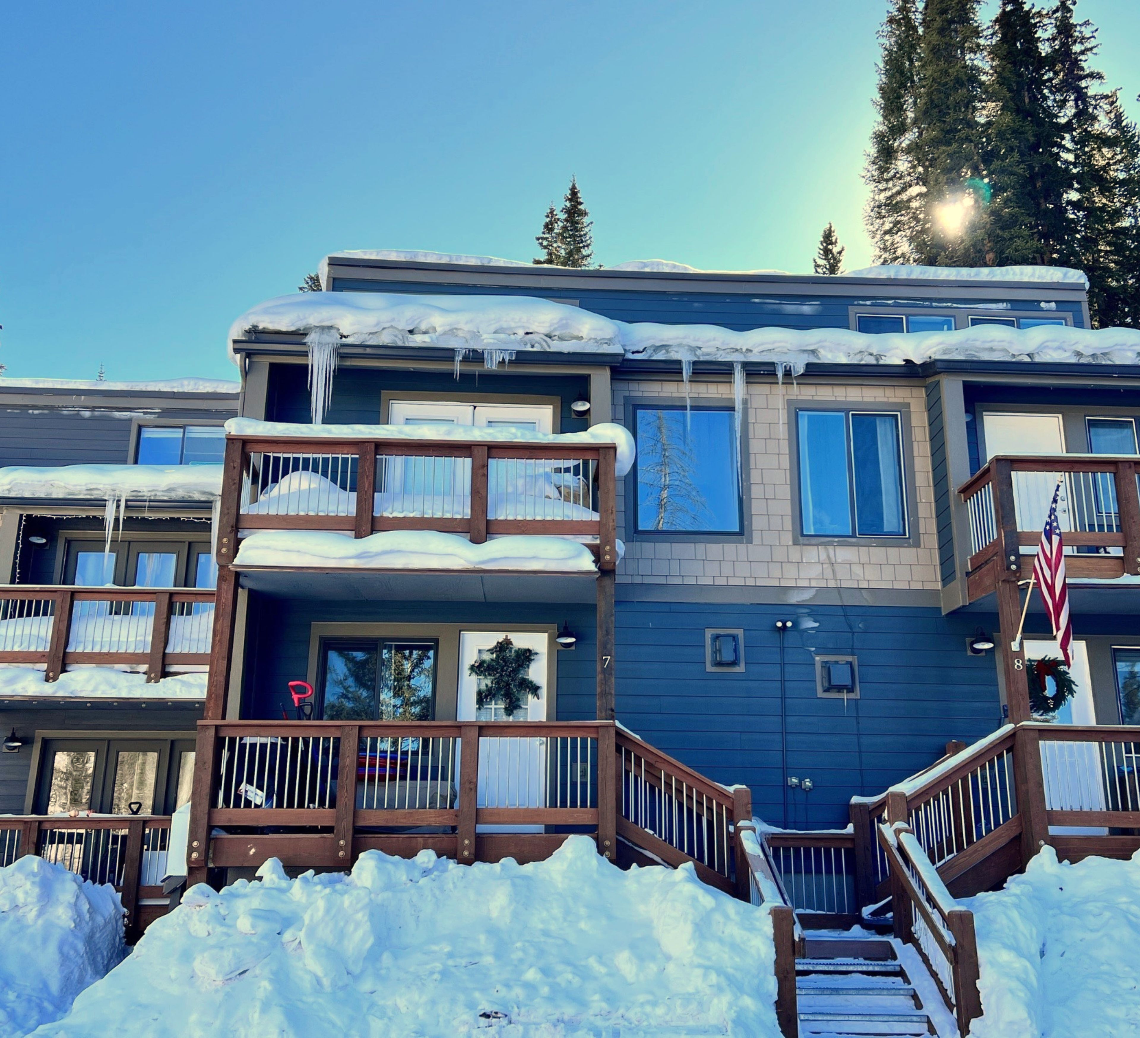 A multi-story building with balconies and a wooden deck, surrounded by snow.