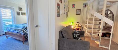 Un dormitorio con una cama, un sofá gris, una escalera y una pared con varias imágenes.