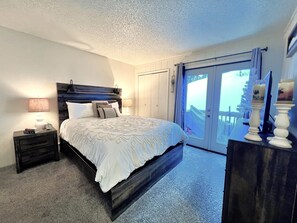 Ein Schlafzimmer mit Bett, Nachttischen, einem Schminktisch und Blick ins Freie durch eine Schiebetür.