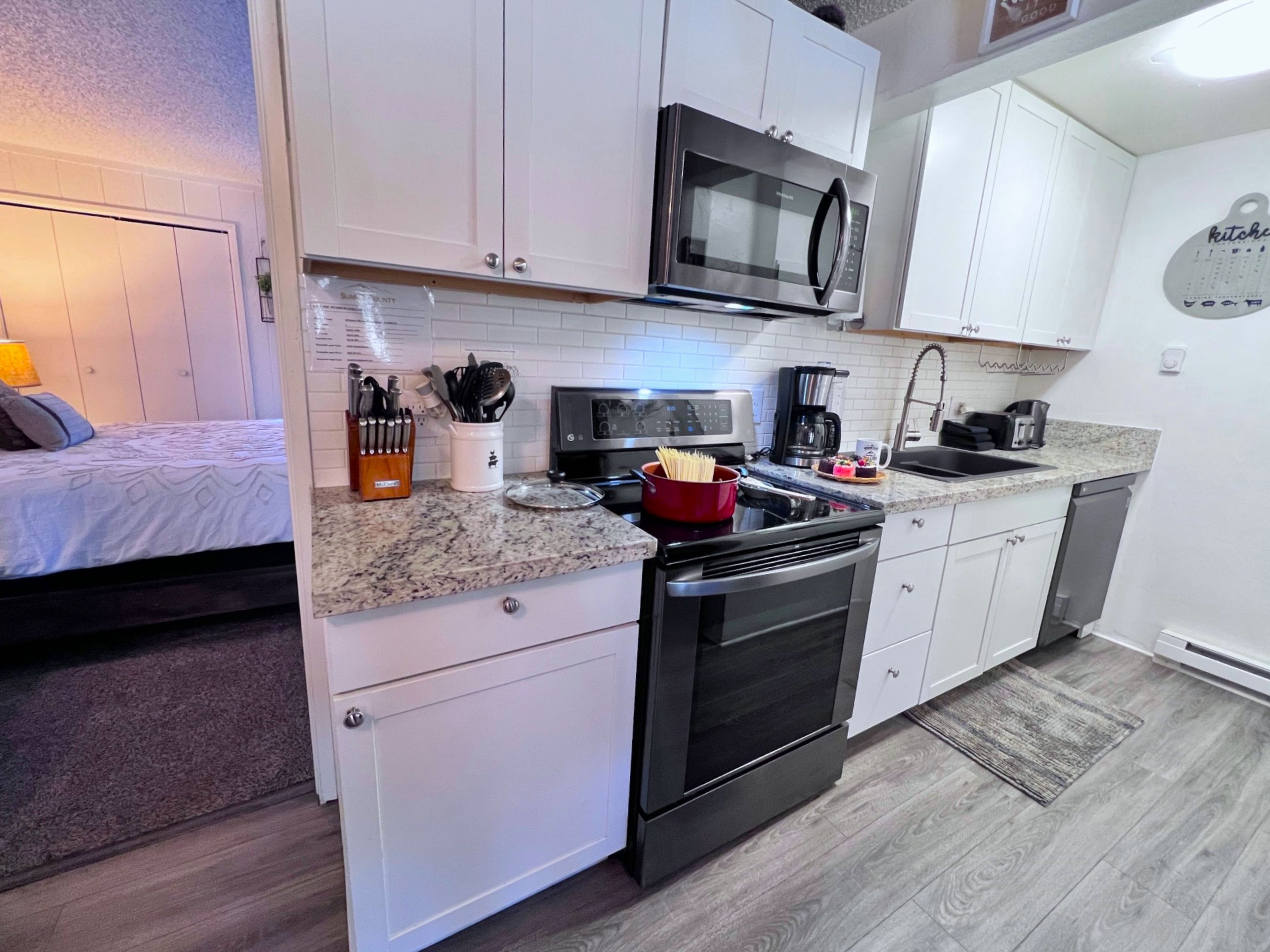 A compact kitchen with white cabinets, a microwave, a stove, and a coffee maker.