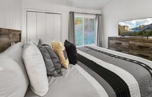 Ein Schlafzimmer mit einem Bett, einem Schminktisch, einem Fernseher und Blick auf eine Berglandschaft.