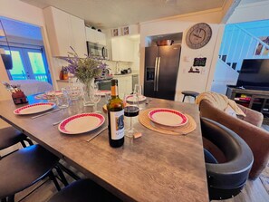 A dining area with a wooden table set for two, a bottle of wine, and a vase with flowers.