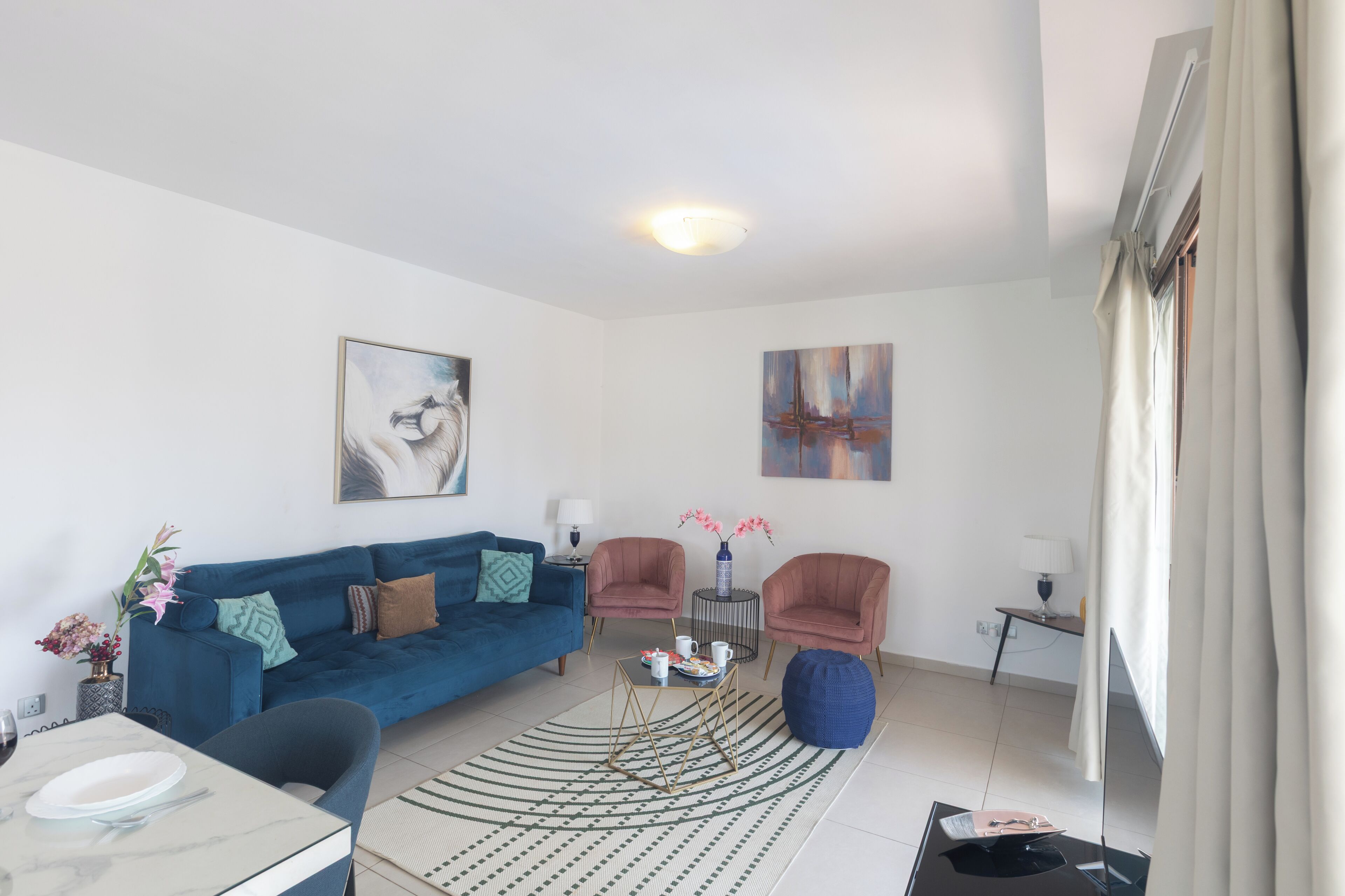 En moderne stue med en blå sofa, to lænestole, et sofabord og et spiseområde med bord og stole.