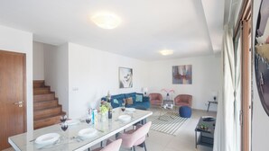 A modern living room with a dining area, a staircase, and a sofa set.