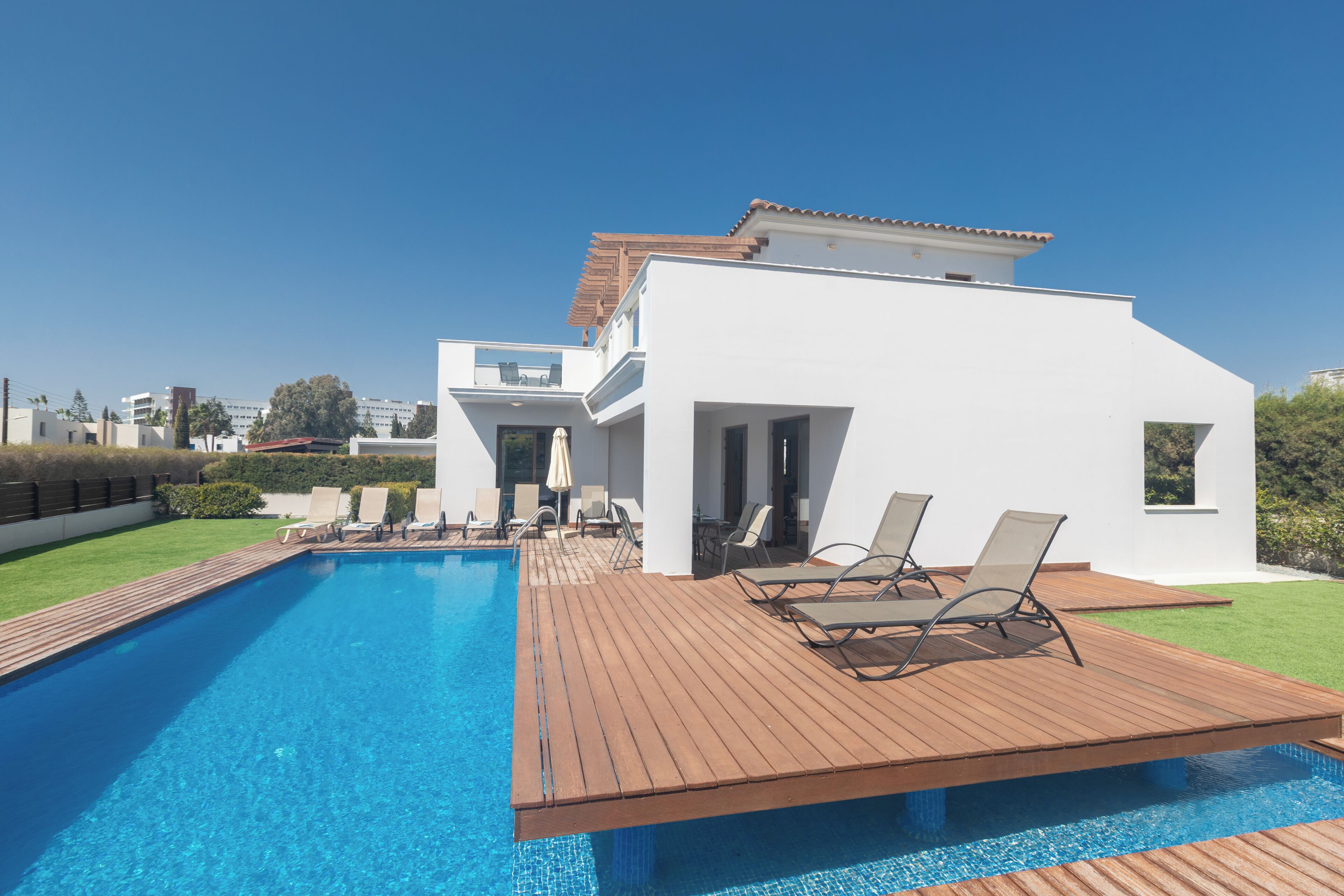 A modern house with a swimming pool, wooden deck, and lounge chairs.