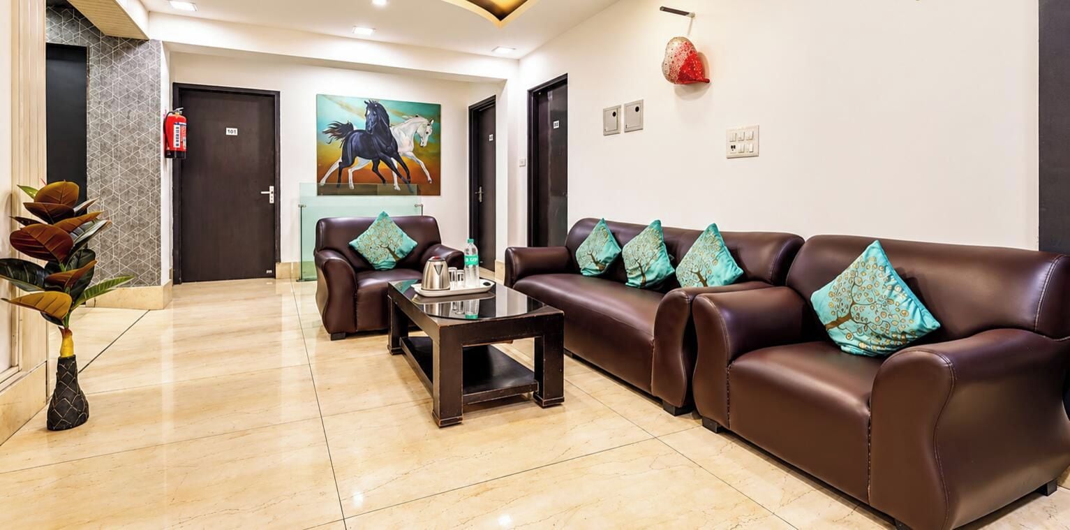 A hotel lobby with a reception desk, two sofas with patterned cushions, a coffee table, and a painting of horses on the wall.