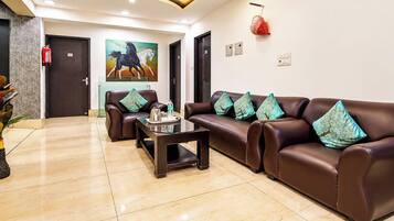 A hotel lobby with a reception desk, two sofas with patterned cushions, a coffee table, and a painting of horses on the wall.
