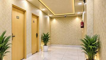 A hotel corridor with two wooden doors, each marked with a number, and potted plants on either side.
