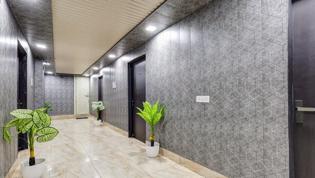 A hallway with tiled walls, a marble floor, and potted plants. - Mauryan Signature hotel Devli Khanpur (New Delhi)