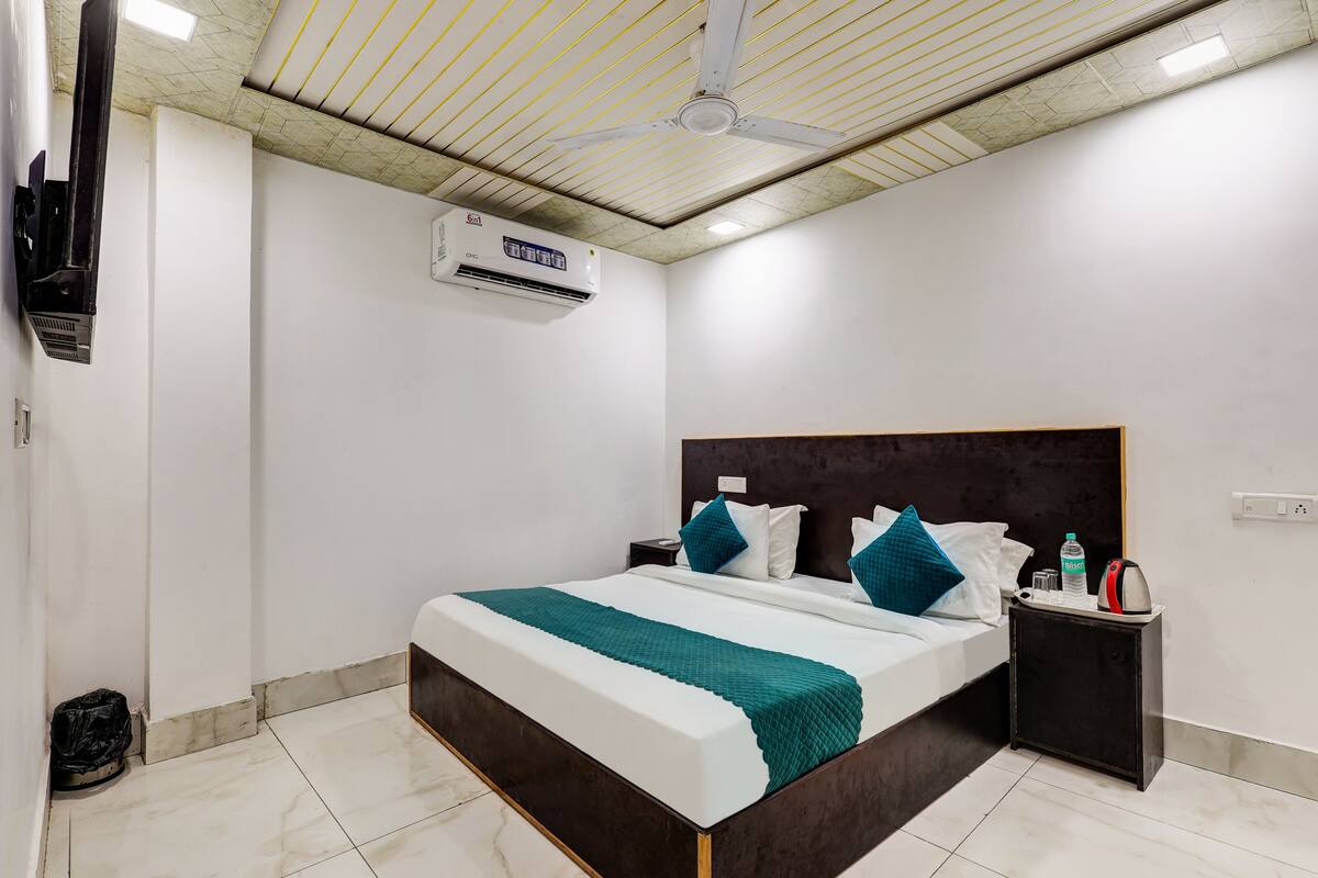 A modern hotel room with a large bed, a nightstand, a wall-mounted air conditioner, and a ceiling fan.