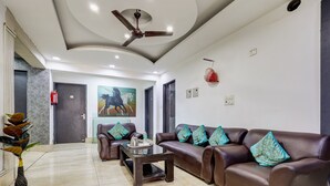 A modern living room with a brown leather sofa set, a coffee table, and a painting of horses. - Mauryan Signature hotel Devli Khanpur (New Delhi)