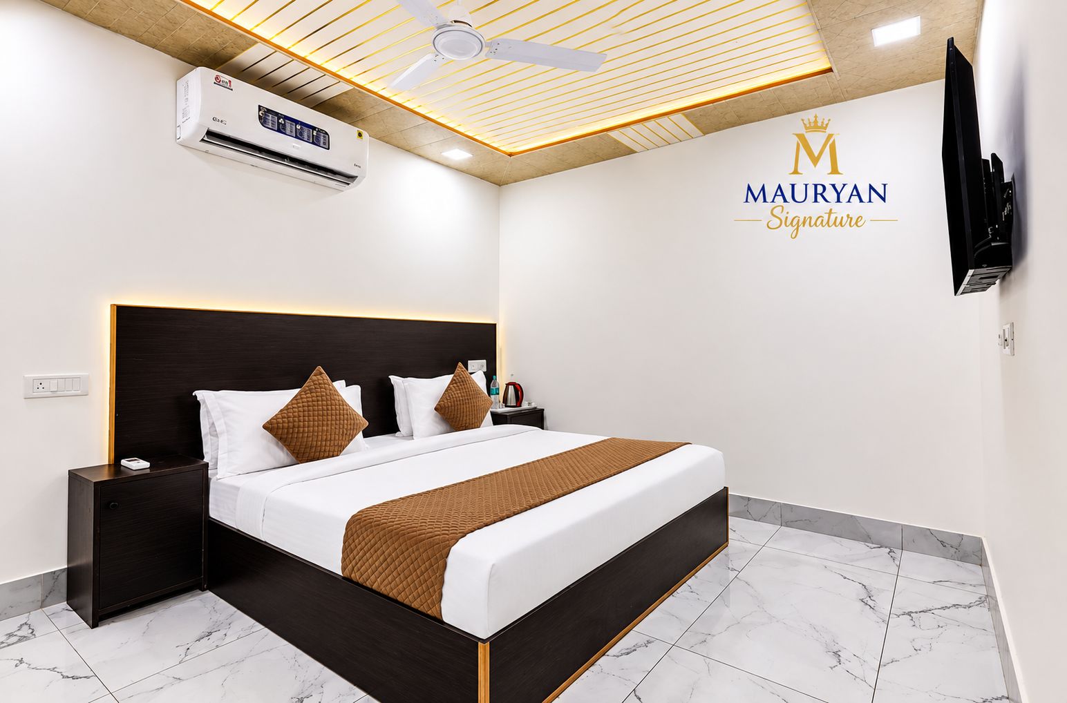 A modern hotel room with a large bed, a ceiling fan, an air conditioning unit, and a television.