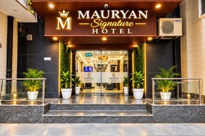 The exterior of the Mauryan Signature Hotel with a prominent entrance, potted plants, and a sign indicating the hotel name.