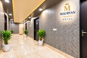 A hotel corridor with potted plants, a reception area, and a sign for 'MAURYAN Signature Hotel'.