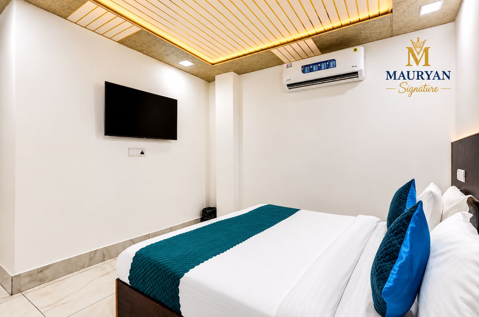 A hotel room with a bed, a flat-screen TV, an air conditioning unit, and a logo on the wall.